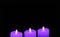 Shining three purple candles on black background