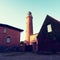 Shinning old lighthouse above houses before sunset. Tower illuminated with strong warning light