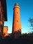 Shinning old lighthouse above houses before sunset. Tower illuminated with strong warning light