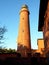 Shinning old lighthouse above houses before sunset. Tower illuminated with strong warning light