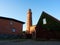 Shinning old lighthouse above houses before sunset. Tower illuminated with strong warning light