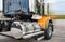 Shiny big rig semi truck tractor in black and orange with polisher aluminum fuel tanks and steps and another accessories ready to
