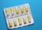 shiny blister tablets yellow-white in the form of capsules on a blue background, top view