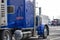 Shiny blue classic big rig semi truck with lot of chrome accessories with semi trailer standing on the parking lot of big truck