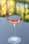 Shiny clean wine glass with pink-coloured rose wine reflecting spears of a surrounding fence standing on a gray table in a cafe