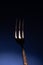 Shiny metal fork with three prongs on blue