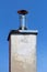 Shiny metal new small chimney with metal cap and lightning rod on top of dilapidated concrete foundation with cracked facade