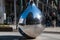 Shiny stainless steel tear drop shaped sculpture seen on a street in Manhattan New York. There is a reflection of a large building