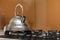 Shiny stainless tea kettle teapot with boiling water on gas stove on kitchen yellow copy space background