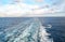 Ship`s wake behind a cruise ship. Cloudy blue sky background.