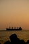 Ship sitting on top of the ocean at sunset near rocks