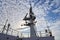 Ship structures, masts, antennas, funnel, ship wheelhouse against the blue sky and clouds.