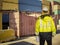 Ship supervisor engineer inspector stands at the dockside in a port. Wearing safety helmet and yellow vest. Cargo shipping