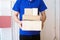 The shipper in the blue suit holds a brown box standing in front of the customer house. Free shipping for online shopping and