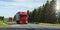 Shipping two red cargo trucks on the road being driven sun rays