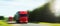 Shipping two red cargo trucks on the road being driven sun rays speed motion blurred background