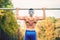 Shirtless handsome man doing chin ups in park, wearing an anonymus mask. Fitness player, personal trainer working out in park