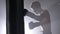 Shirtless kickboxer silhouette boxing punching bag as exercise, training in dark room with smoke