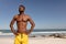 Shirtless man with hands on hip and eyes closed standing on beach in the sunshine