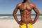 Shirtless man with hands on hip standing on beach in the sunshine