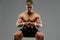 Shirtless muscular guy sits on white box and holds barbell weigh