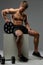 Shirtless muscular guy sits on white box and holds barbell weigh