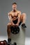 Shirtless muscular guy sits on white box and holds barbell weigh