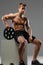 Shirtless muscular guy sits on white box and holds barbell weigh