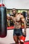 Shirtless muscular male boxer resting next to punching bag