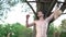 Shirtless muscular man putting on wireless earbuds and exercising pull up on tree