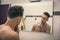 Shirtless young man examining his face in bathroom mirror