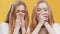 Shock reaction. Two redhead twin sister feeling amazed and stunned, covering their mouths, orange background