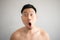 Shock and surprise face of Asian man in topless portrait isolated on gray background