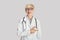 Shocked adult woman in white coat, glasses with stethoscope with open mouth points finger to empty space