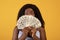 Shocked African American woman covering her face with money, showing shopping budget on orange background