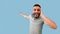 Shocked arab guy grabbing his head and pointing at blank space with open mouth, offering huge discounts, blue background