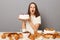 Shocked astonished surprised woman wearing white T-shirt isolated over gray background holding big cake sitting at festive table