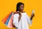 Shocked black shopaholic lady looking at smartphone and holding lots shopping bags