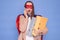 Shocked brown haired woman wearing superhero costume holding documents in folders posing isolated over blue background talking on