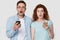 Shocked couple holds cell phones looking at camera pose indoors