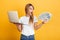 Shocked emotional young blonde woman posing  over yellow wall background dressed in white casual t-shirt using laptop