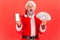 Shocked excited gray bearded man in santa claus costume holding fan of dollars and white screen smartphone, online banking,