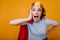 Shocked girl in paper crown fooling around during indoor photoshoot. Studio shot of surprised woman in superhero costume