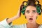Shocked Housewife With Curlers Touching Head Posing On Yellow Background