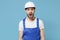 Shocked irritated young man in coveralls protective helmet hardhat isolated on blue background. Instruments accessories