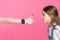 Shocked little girl looking at woman with smartwatch showing thumb up