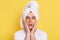 Shocked man wrapped towel on head doing morning cosmetology procedures, keeps palms on cheeks, looking at camera with big eyes,
