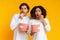 Shocked multiracial couple holding popcorn buckets and looking at camera