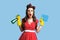 Shocked pinup woman in red polka dot dress holding detergent and rag, shouting OMG on blue studio background