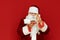 Shocked santa claus looks at burger in hand isolated on red background. Man in santa costume eating fast food on red background.